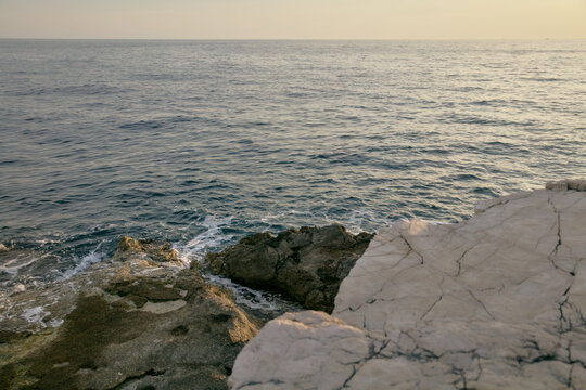Calm sea water washing against rocky white limestone cliff shoreline at sunset
