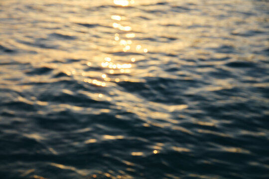 Abstract blurred water surface with golden sunlight reflections at sunset blurred