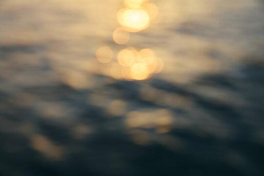 Abstract golden bokeh light reflections on dark sea water surface at sunset