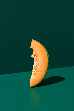 Minimal still life of cantaloupe wedge on green backdrop