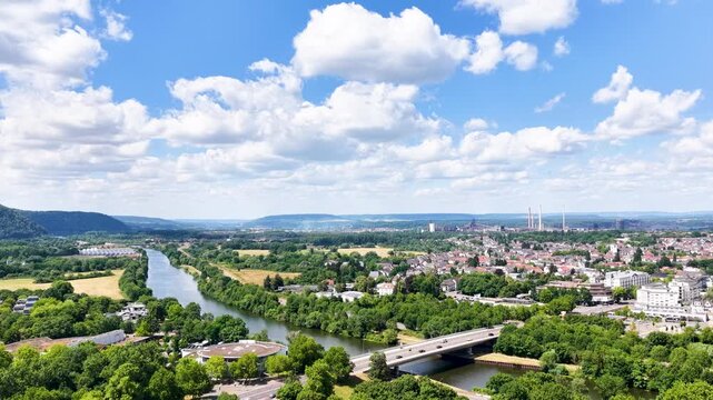 Vogelperspektive auf Saarlouis mit der vorbeiflie&szlig;enden Saar, einer markanten Stra&szlig;enbr&uuml;cke, dichter gr&uuml;ner Vegetation und der Stadtlandschaft unter blauem Wolkenhimmel.