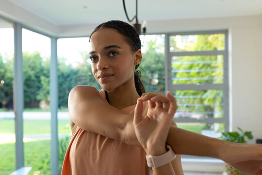 Adult African woman stretching right arm across chest at home in sleeveless top, smartwatch visible