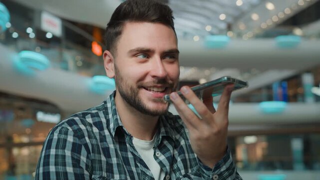 Caucasian happy smiling male man recording voice mail with mobile phone in shopping mall carefree guy record audio message with easy smartphone command enjoying virtual communication with cellphone