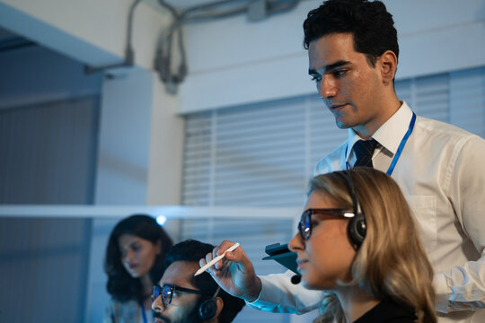 Manager mentor customer service agents wearing headsets in a control room. Corporate training, IT helpdesk supervision, professional support staff, and late night call center 
