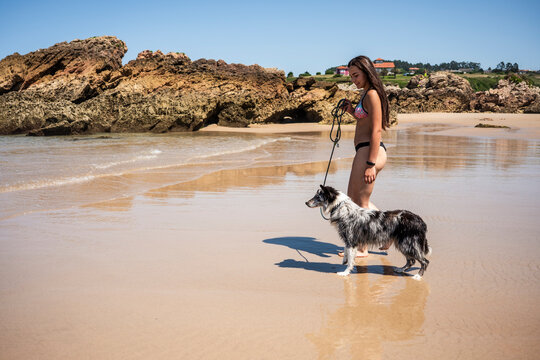Woman walking dog on quiet beach near rocky coastline