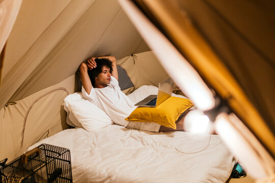 Man relaxing alone in tent with laptop on camping bed