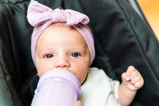 Close-up baby girl with pink bow drinking from bottle