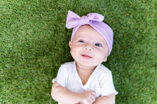 Smiling baby in purple head wrap lying on green grass