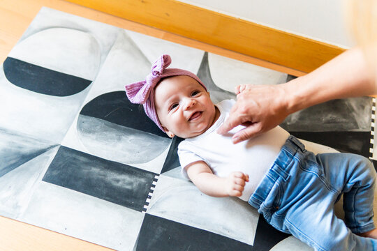 Smiling baby girl on patterned mat with mother hand