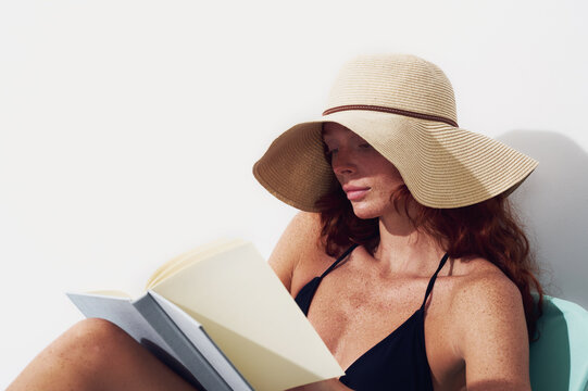 Woman relaxing poolside reading book in summer sun