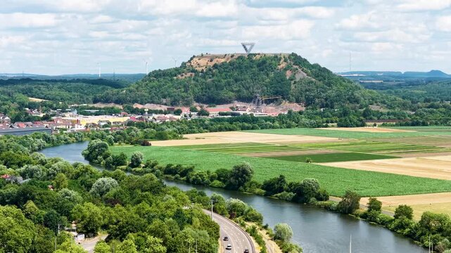Vogelperspektive auf Saarlouis mit der vorbeiflie&szlig;enden Saar, einer markanten Stra&szlig;enbr&uuml;cke, dichter gr&uuml;ner Vegetation und der Stadtlandschaft unter blauem Wolkenhimmel.