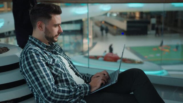 Gadget addicted Caucasian man freelancer student male working with laptop distant in business center focused male guy work studying with computer e-learning online ordering purchases in shopping mall