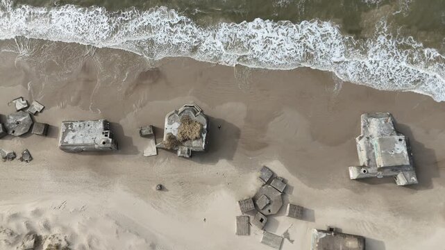 Top-down drone footage of abandoned military bunkers on a Danish beach, with waves moving across the shoreline. Ideal for military history, coastal erosion, World War II heritage and documentary theme