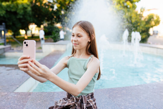 Teenage girl taking selfie by fountain in city park