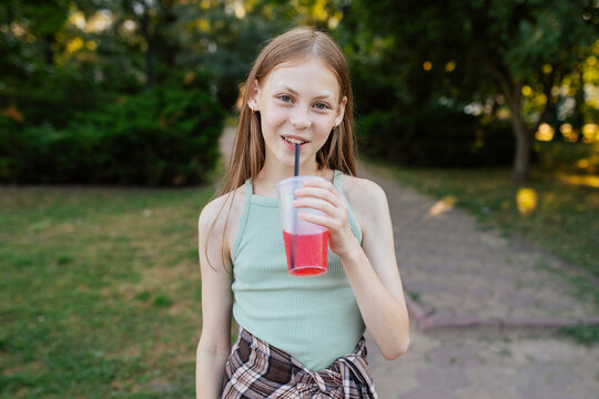 Teen girl drinking cold fruit juice outdoors in summer park