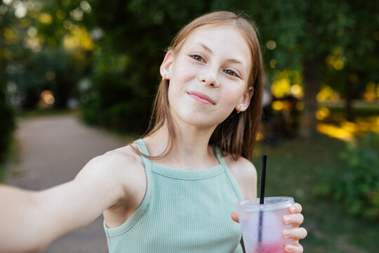 Teenage girl taking selfie with cold drink in park