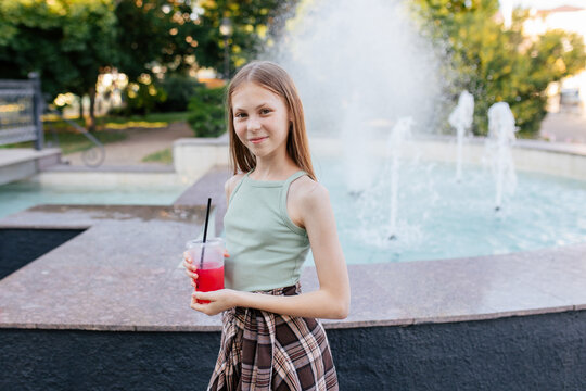 Teenage girl with cold drink standing near park fountain
