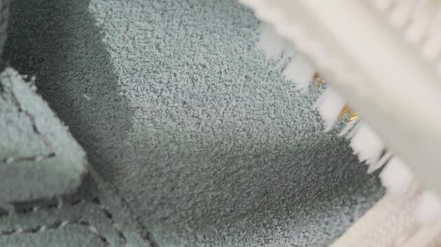 Natural light highlights detailed cleaning of soft suede footwear. Brushing green suede sneaker gently emphasizes repairs and natural textures in detail