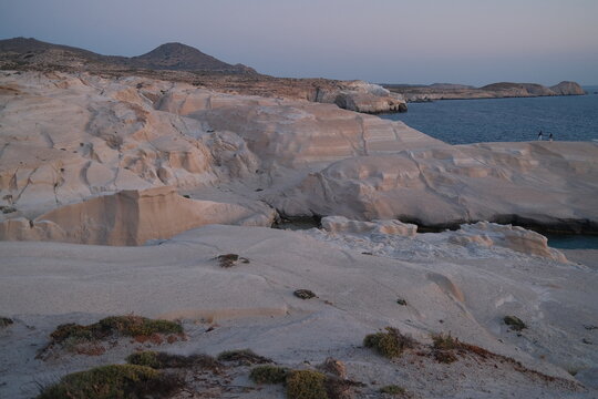 Expansive view of Sarakiniko Beach in Milos, Greece, featuring white volcanic rock formations bathed in soft sunrise light beside the blue Aegean Sea.