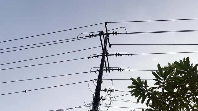 Silhouette of utility pole with messy power lines against blue sky