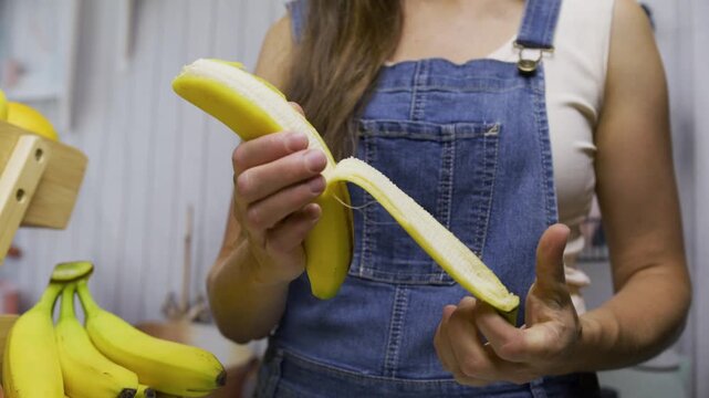 Woman peeling banana and cutting it on board with knife - closeup, slow motion shot