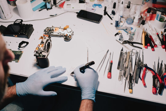 Camera repair technician documenting a disassembled digital camera and components at a precision electronics service workbench