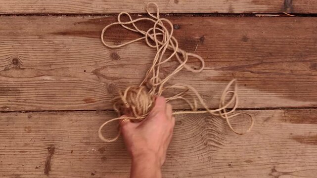 Woman removes a coil of natural jute rope from rustic wooden boards, handmade materials, eco packaging, craft supplies, natural texture.