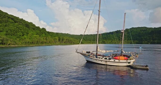 Sailboat anchored in tranquil bay of crystal blue water surrounded by lush tropical rainforest, representing adventure, remote travel, and exploring pristine natural beauty of Torres islands, Vanuatu