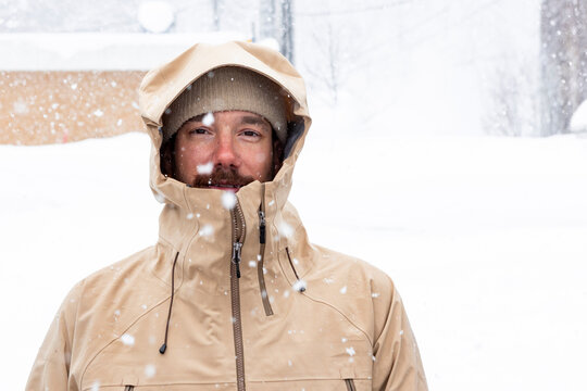 Man in hooded parka standing outdoors during snowfall