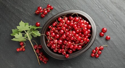 Fresh red currants and green leaves on dark grey textured table, flat lay © New Africa