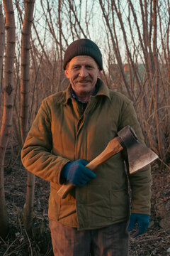 Smiling senior man holding an axe on his shoulder in the garden close up
