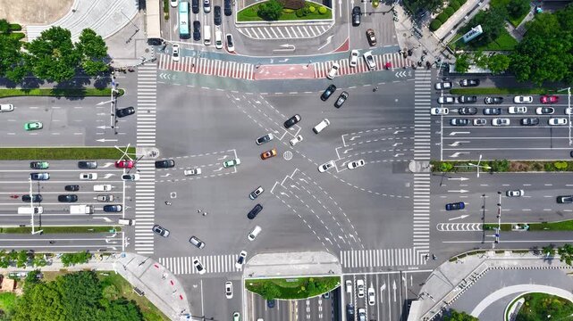 Top-down aerial view of busy urban road intersection with moving vehicles and zebra crossings