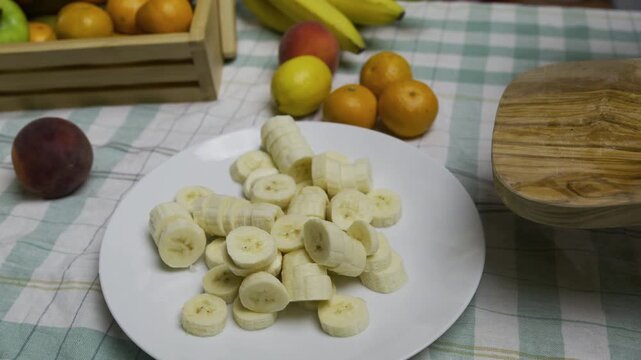 Chef using knife to push banana slices off cutting board and onto plate - slow motion, high shot