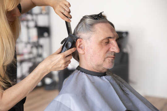 Hairdresser trims the hair of a mature man with clippers at a salon