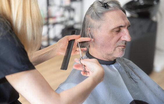 Hairdresser cuts the hair of a senior man in a beauty salon