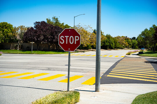 Red stop sign at a suburban intersection with yellow crosswalk markings