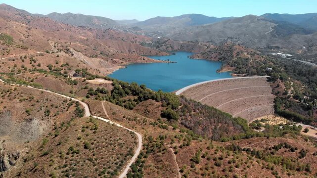 Aerial drone view of Embalse del Limonero dam and reservoir in Malaga, Spain, showcasing vast water storage infrastructure against arid mountains, conveying environmental engineering and resource mana