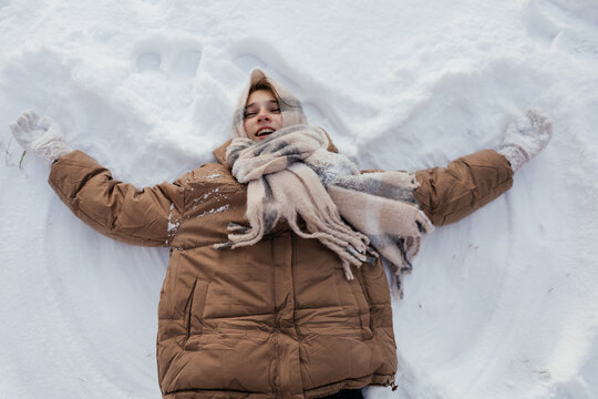 Young girl making snow angel in winter coat and scarf