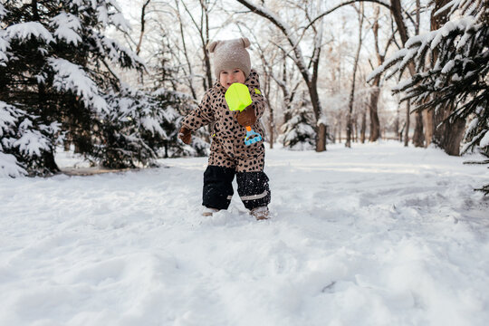 Toddler playing in snowy park with toy shovel in winter