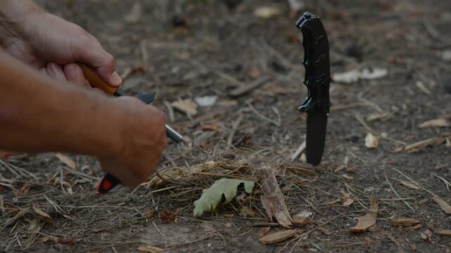 Bushcraft survivalist striking sparks with ferro rod fire steel to ignite tinder on ground at forest campsite with natural outdoor ambient soundscape for wilderness survival. 
