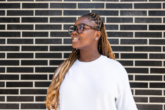 Smiling Black woman with braids and glasses by brick wall