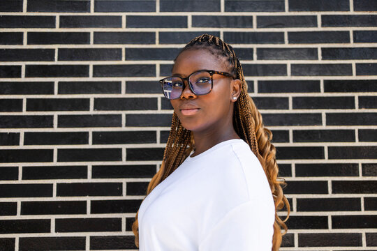 Confident Black woman with braids and glasses by brick wall