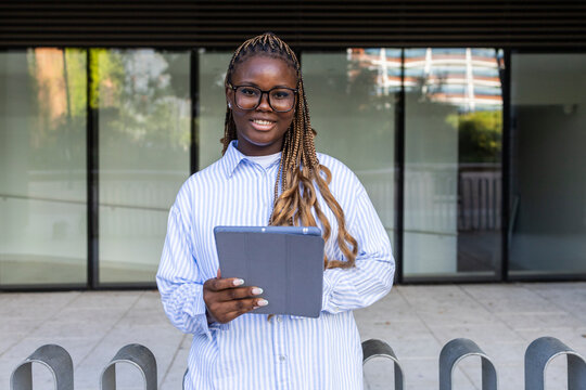 Smiling Black woman with braids holding tablet outdoors