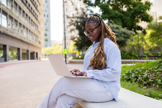 Black woman with braids using laptop on city bench