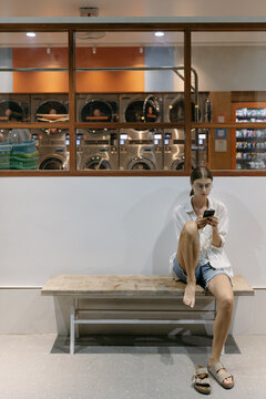 Woman waiting in laundromat using phone