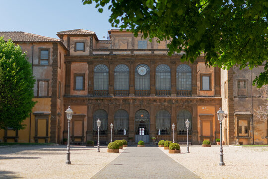 Wide shot of the historic courtyard and grand facade of Villa Mondragone in Italy, featuring a cobblestone walkway and neatly trimmed green topiaries