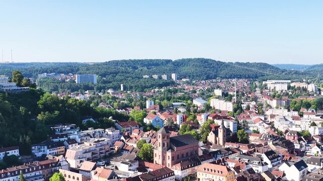 Malerische Ansicht von Homburg an der Saar mit der markanten Stadtkirche, dichten gr&uuml;nen B&auml;umen im Vordergrund und dem bewaldeten Schlossberg unter blauem Sommerhimmel.