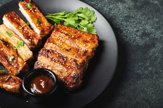 Hot grilled spare ribs from a summer BBQ served on a plate with sauce. Top view. Copy space