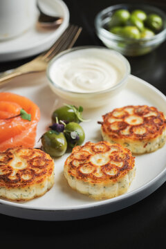 Savory Syrniki with Smoked Salmon, Olives and Sour Cream on White Plate