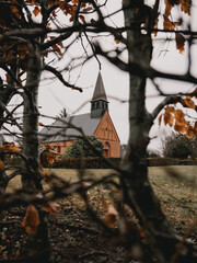 Traditional Danish brick church framed by autumn branches and leaves. Ideal for Scandinavian architecture, rural landscapes, cultural heritage and travel themes. © Pavel